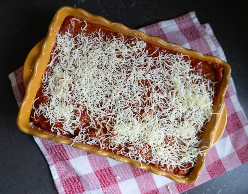 spaghetti pie topped with grated cheese unbaked. in a gold casserole on a red and white kitchen towel on a black kitchen countertop