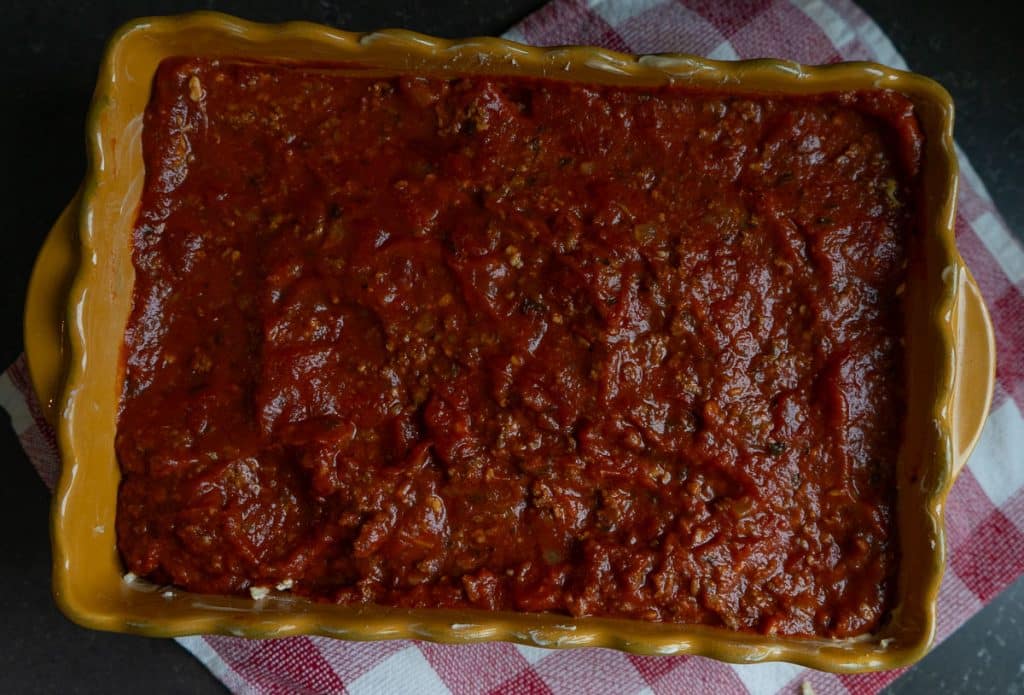 spaghetti cheese layer is covered with spaghetti sauce in a 9x7 gold casserole dish. dish is setting on a red and white kitchen towel the countertop is black