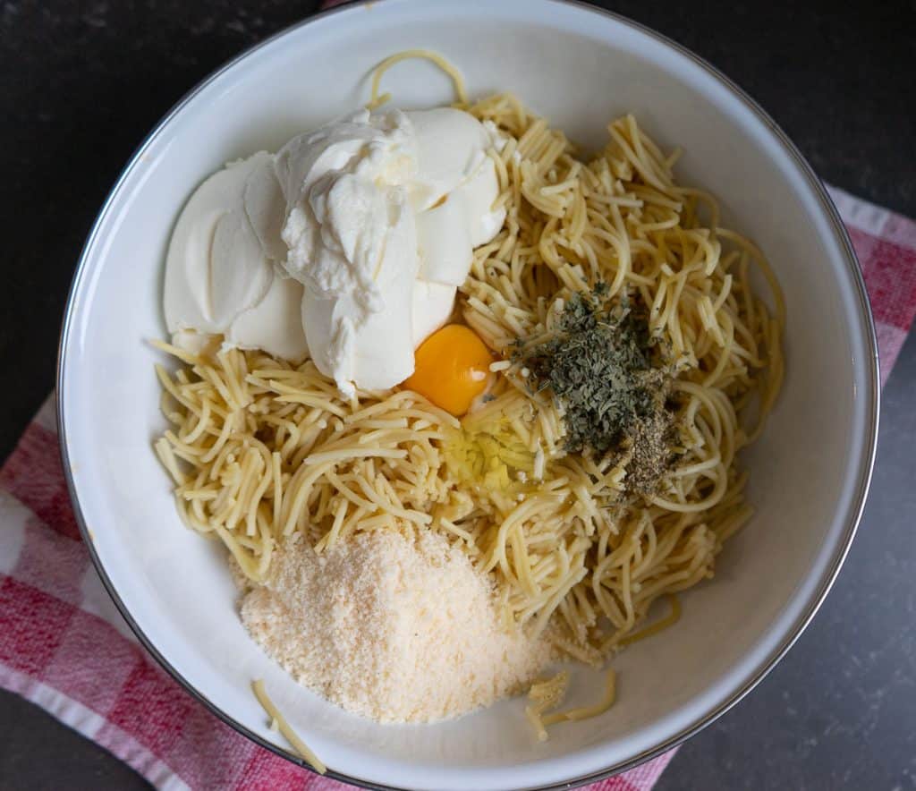 white bowl with spaghetti, egg, cheese, parmesan, pepper, and italian seasoning in it. bowl is sitting on a red and white towel