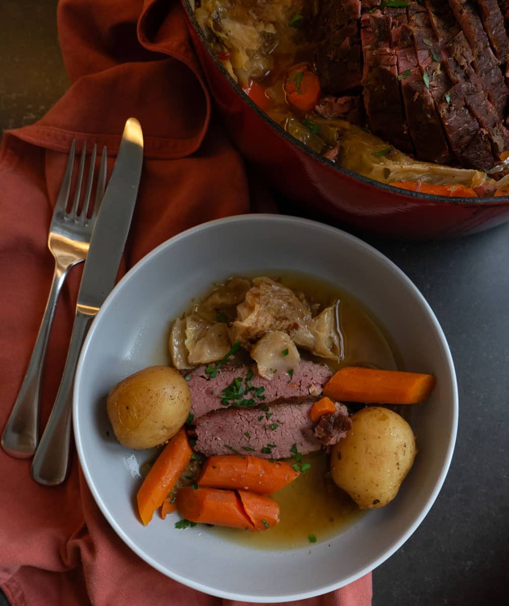 corned beef sliced and served on a gray plate with carrots, potatoes, and cabbage with pan juices