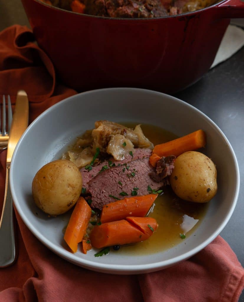 corned beef sliced and served on a gray plate with carrots, potatoes, and cabbage with pan juices