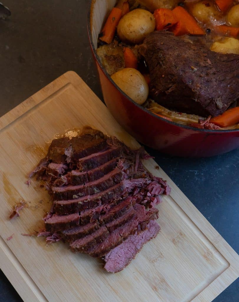 corned beef brisket on a cutting board sliced with pot of boiled dinner next to it