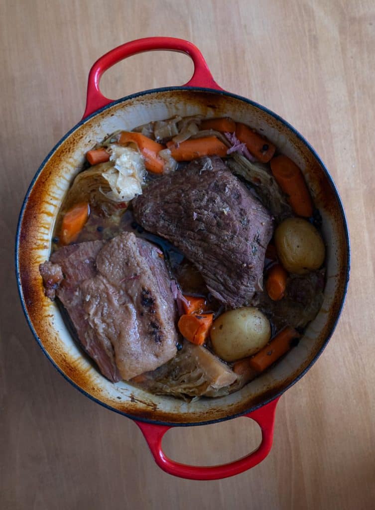 photo of red dutch oven with corned beef and cabbage boiled dinner on a wood tabletop