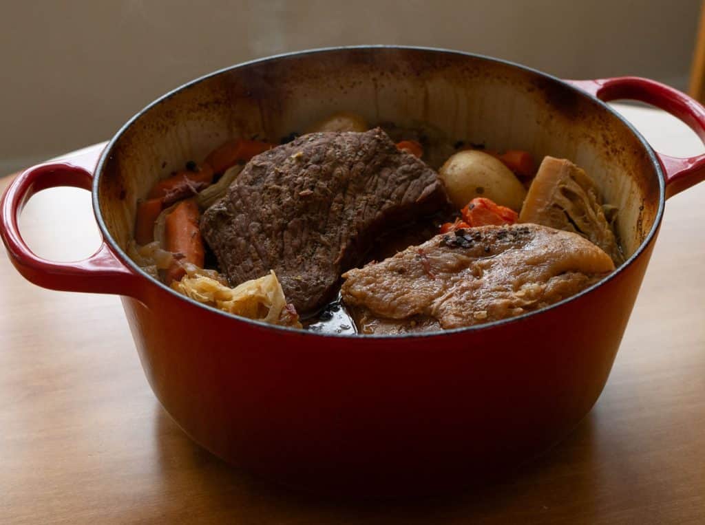 photo of red dutch oven with corned beef and cabbage boiled dinner on a wood tabletop