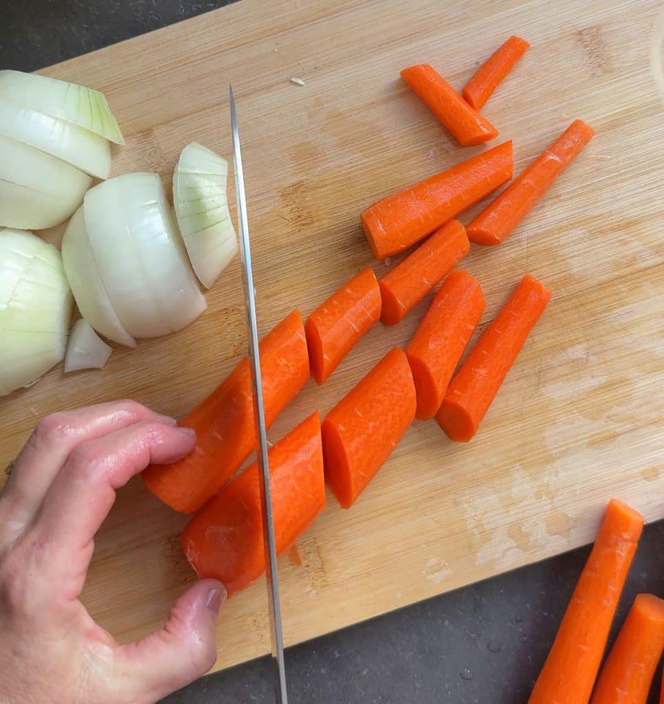 prepping vegetables. cutting carrots and onion is cut in upper left hand corner on a wood cutting board