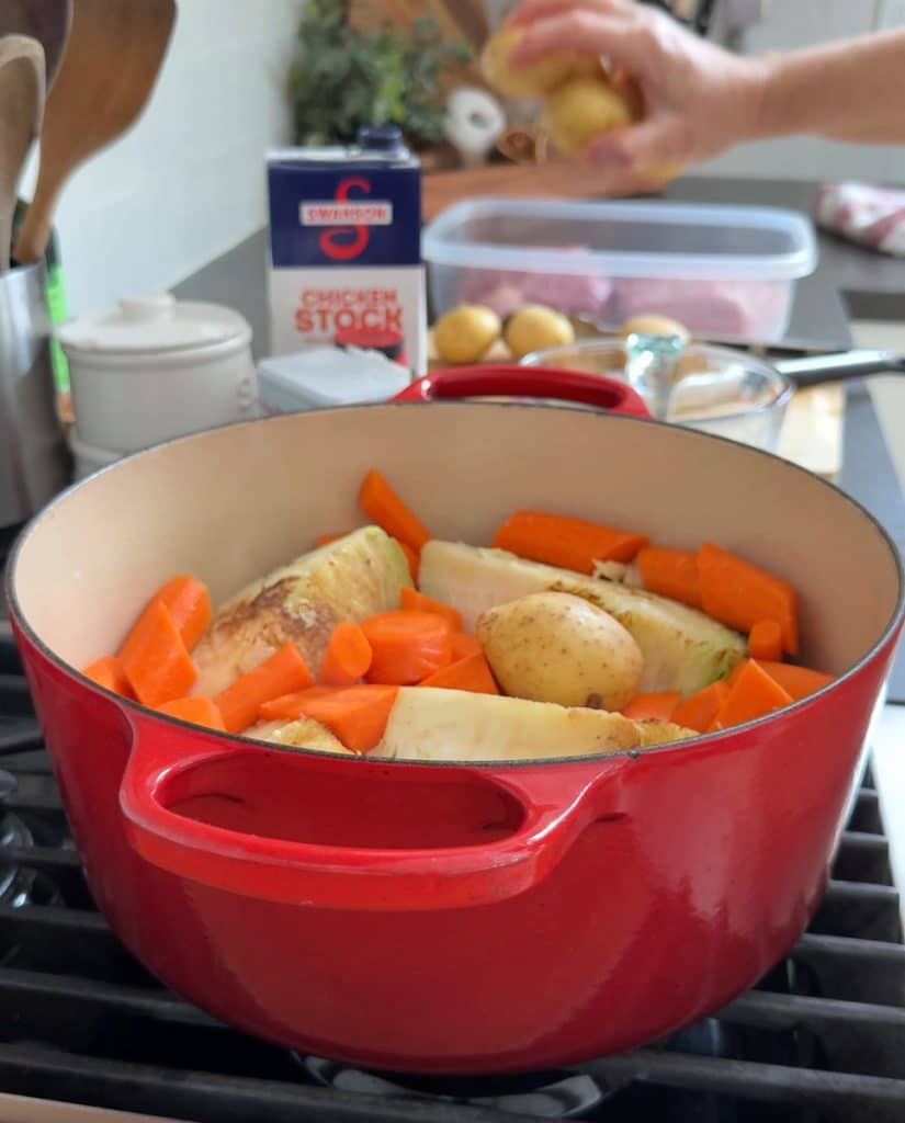 adding carrots and potatoes to dutch oven on stovetop