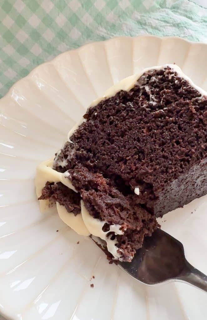 slice of guinness stout chocolate cake on a white plate with a green and white gingham napkin under the plate. fork has cake and frosting on it