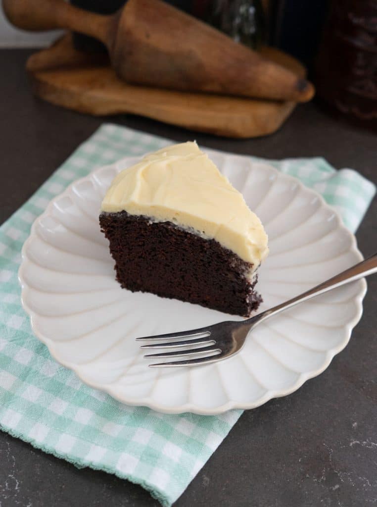 slice of guinness stout chocolate cake on a white plate with a green and white gingham napkin under the plate. fork is on plate