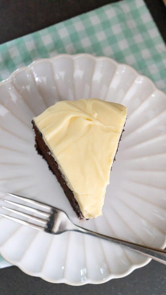 top view of a slice of guinness stout chocolate cake on a white plate with a green and white gingham napkin under the plate. fork is on plate