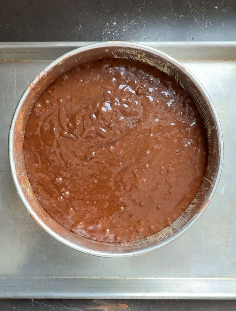 batter in cake pan before being baked cake pan is setting on a silver baking sheet