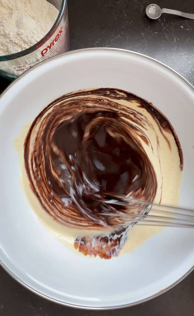 combining wet ingredients in a white bowl and whisking by hand cream and dark chocolate swirling together