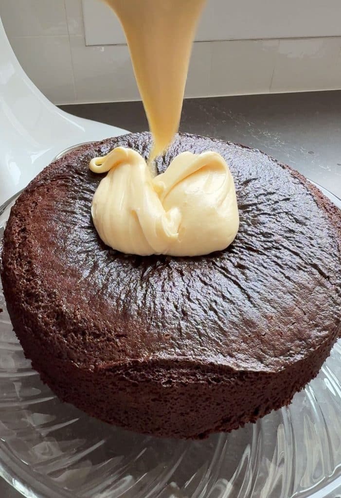 pouring frosting on top of chocolate cake 