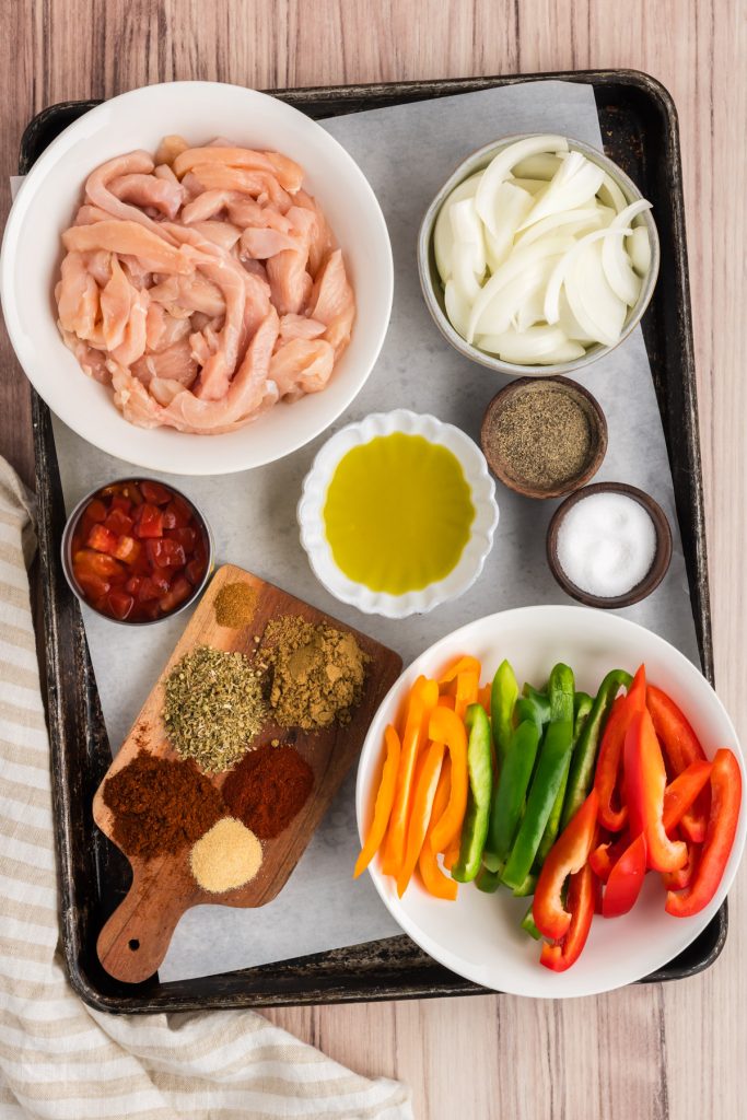 ingredient photo, chicken, bell peppers, onions, oil and spices on a sheet pan