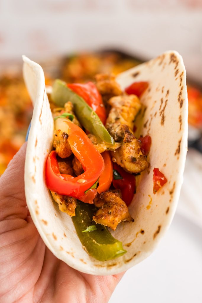 hand holding chicken fajitas in a flour tortilla