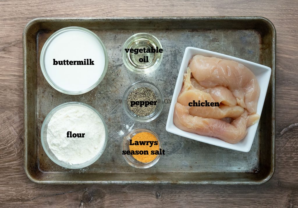 ingredients for chicken tenders on a baking sheet that is on a wood countertop