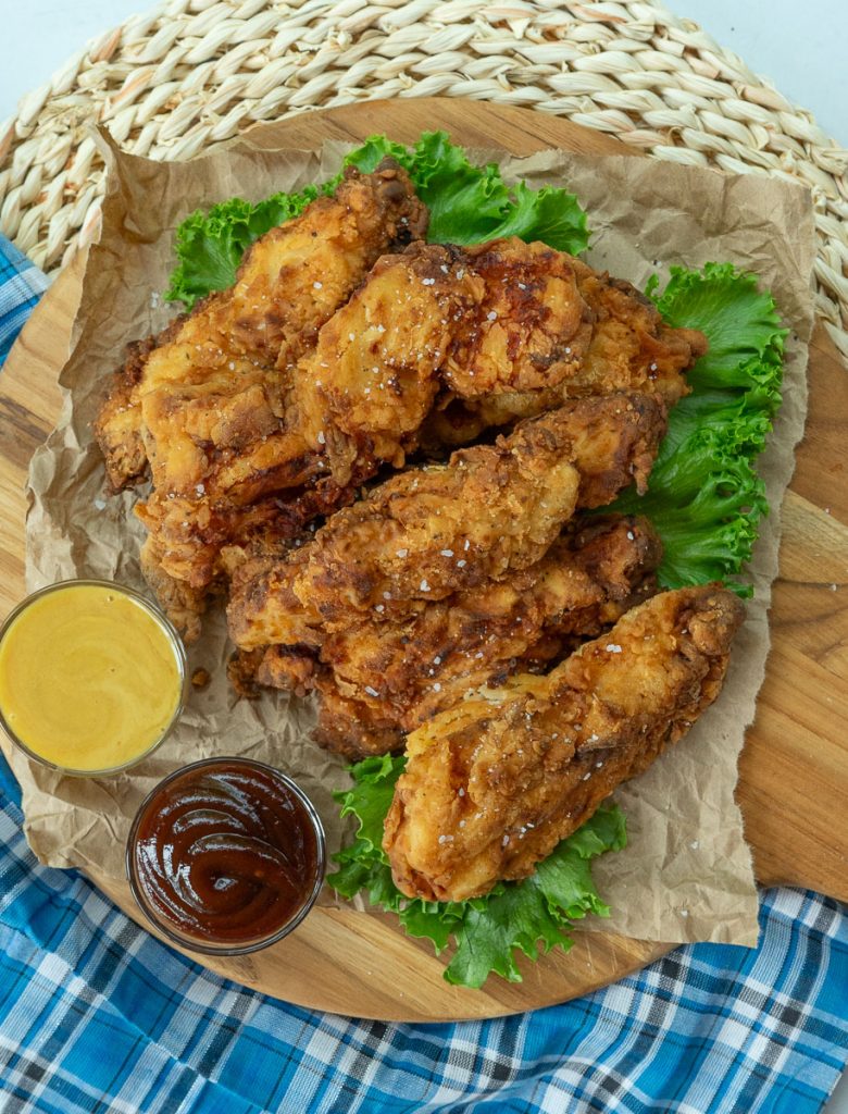 fried chicken strips on a bed of leaf lettuce with two small dishes of dipping sauce on the side