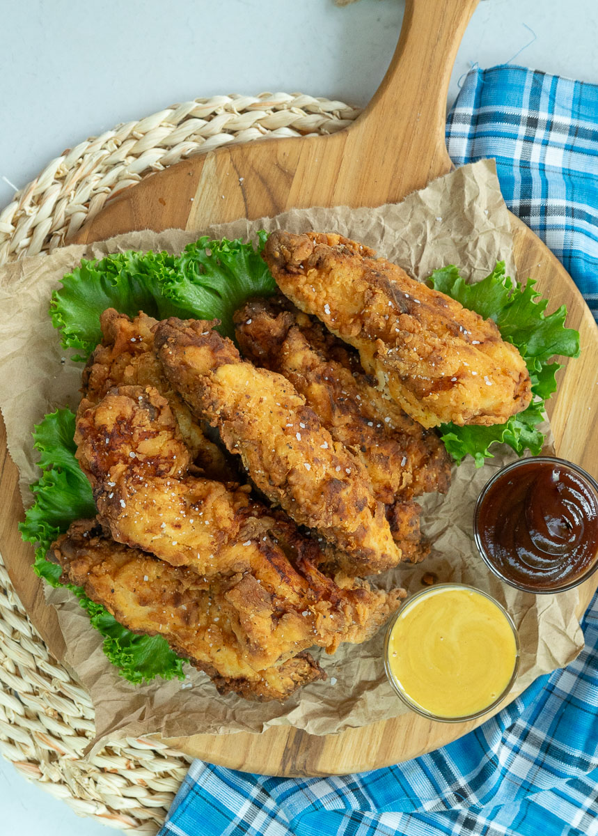 fried chicken tenders on a bed of lettuce with dipping sauces on the side.