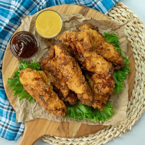 fried chicken tenders on a bed of lettuce with dipping sauces on the side.