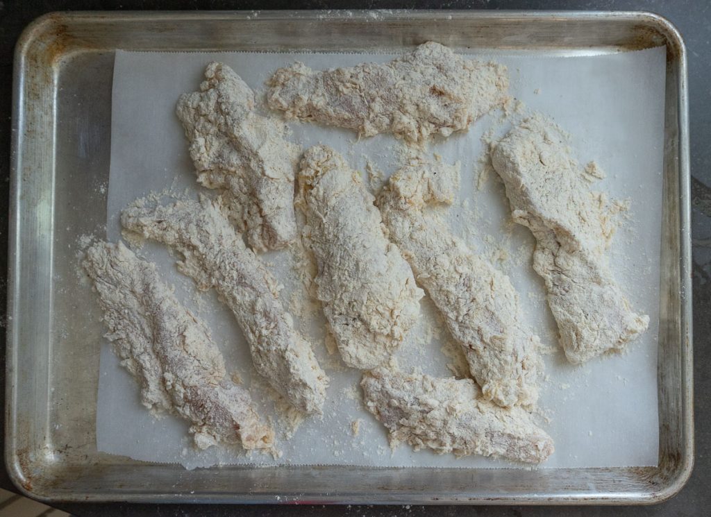 battered chicken tenders before being cooked on a parchment lined baking sheet