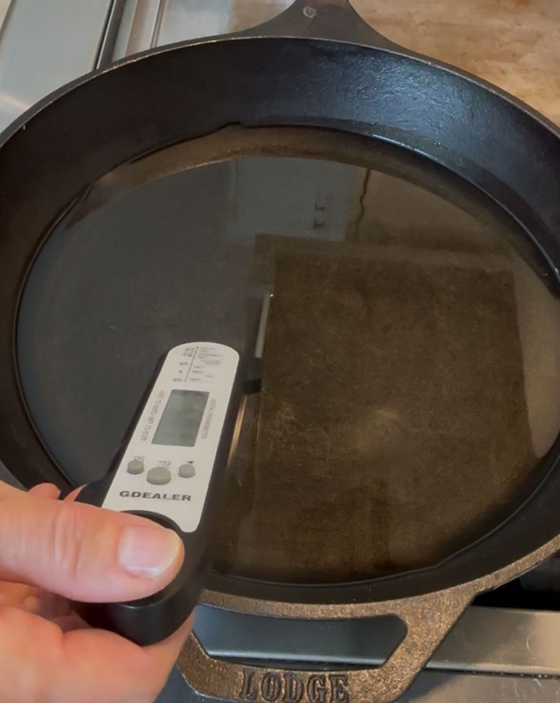 oil in a cast iron skillet with a thermometer checking temperature of the oil