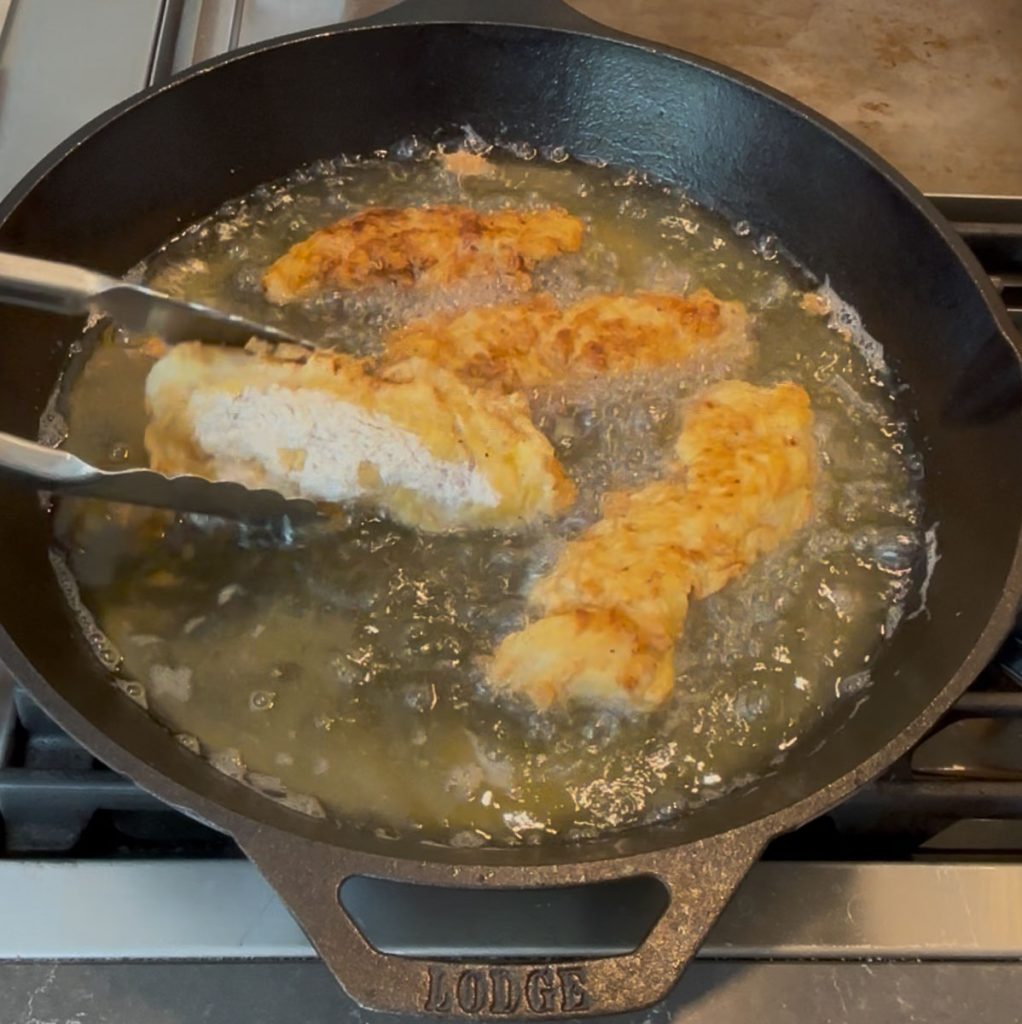 turning frying chicken tenders with metal tongs so they can cook on the other side