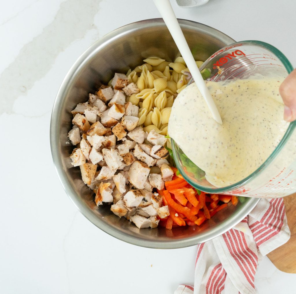 adding pasta salad dressing to the bowl with other ingredients 