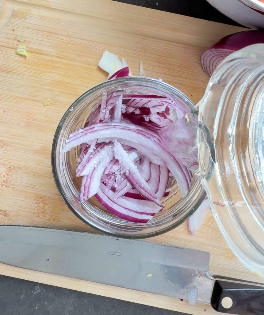 sliced red onion in a pint mason jar on a wood cutting board with a knife laying beside the jar 