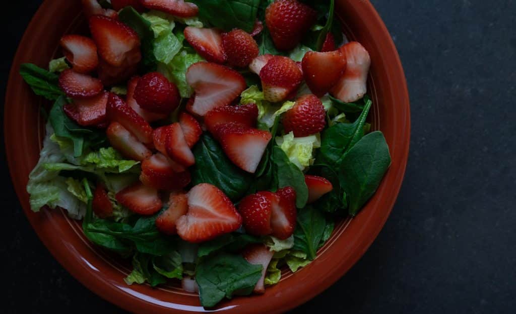 sliced strawberries on top of spinach and romaine in a terra cotta colored bowl