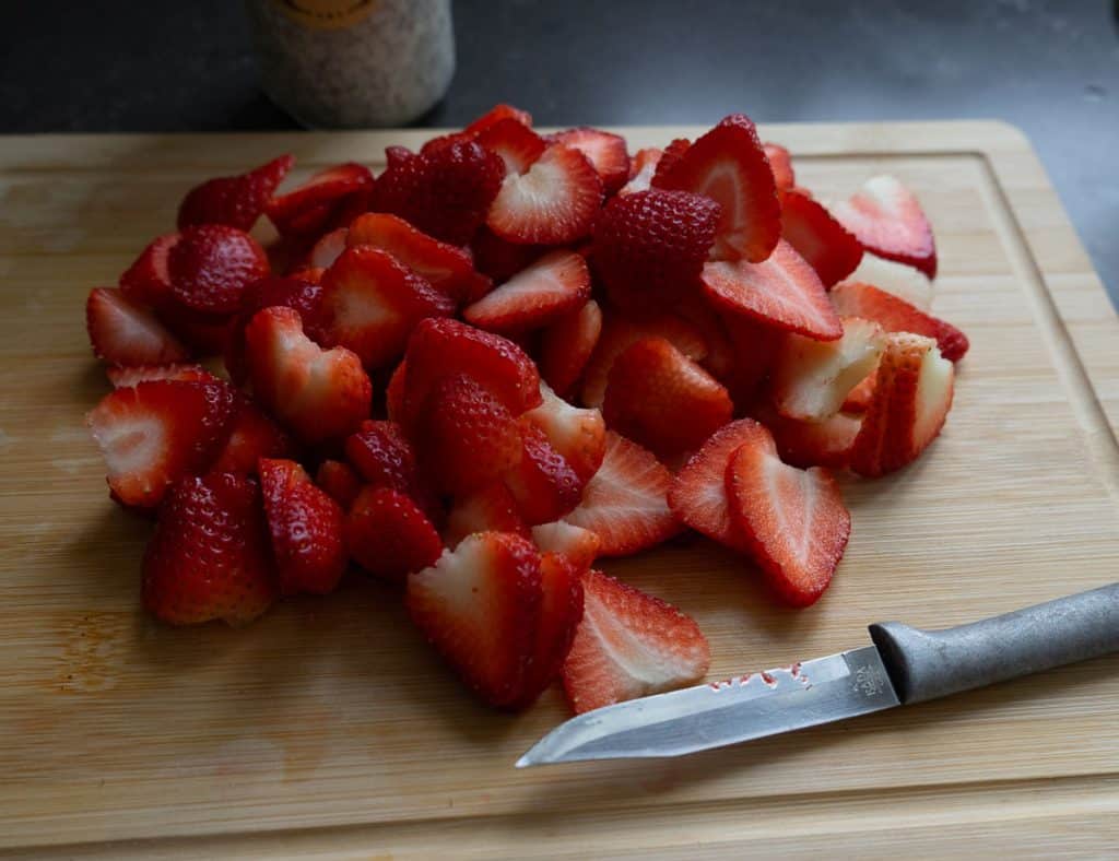 sliced strawberries on a wood cutting board with a parring knife laying in front of the strawberries