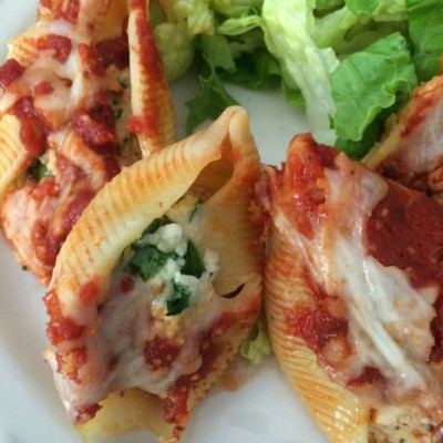Pasta shells stuffed with chicken, spinach and cheese topped with marinara on a white plate with a side salad