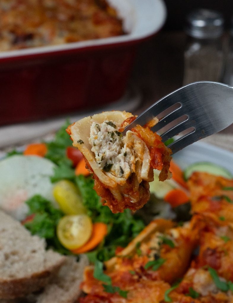 a bite of stuffed spinach and chicken pasta shells on a fork with dinner plate in the background