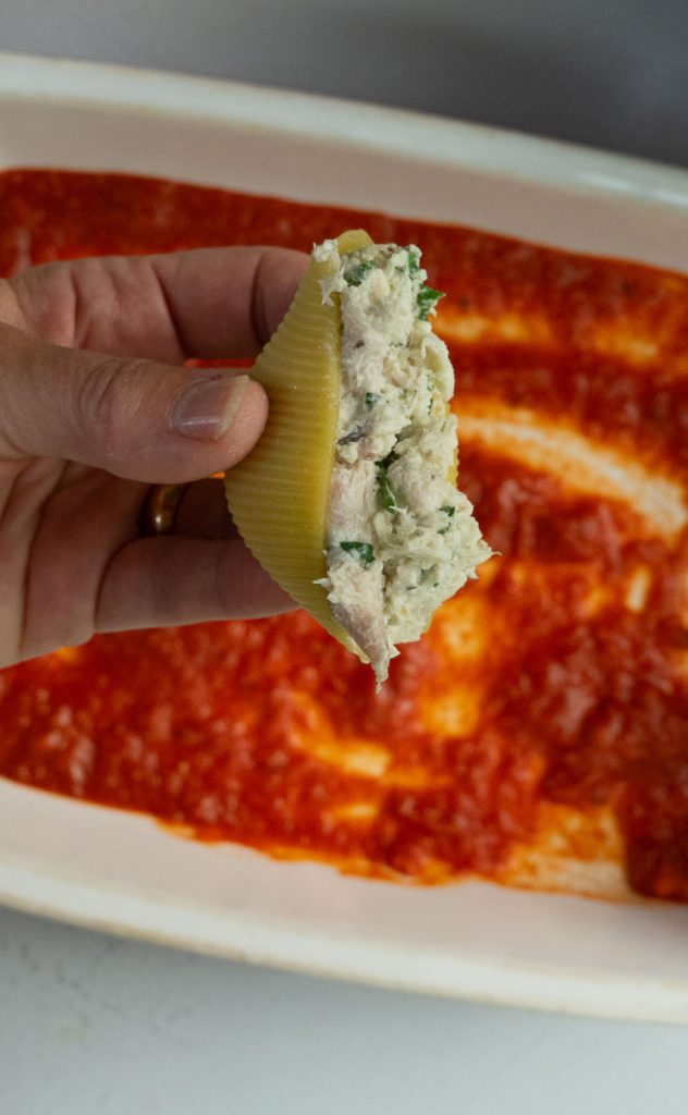 hand holding pasta shell stuffed with chicken and ricotta mixture baking pan is in the background
