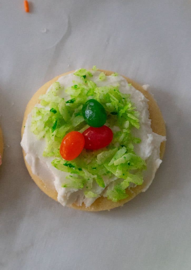 frosted cookies with green colored coconut made into a nest and jelly beans in the center