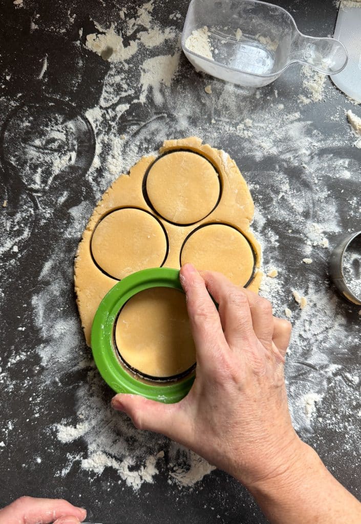 cutting cookies out of rolled out dough with a round cookie cutter on a well floured countertop