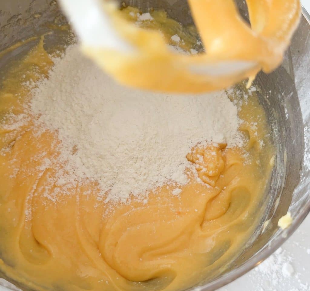 adding dry ingredients to the wet mixture in the bowl of  stand mixer