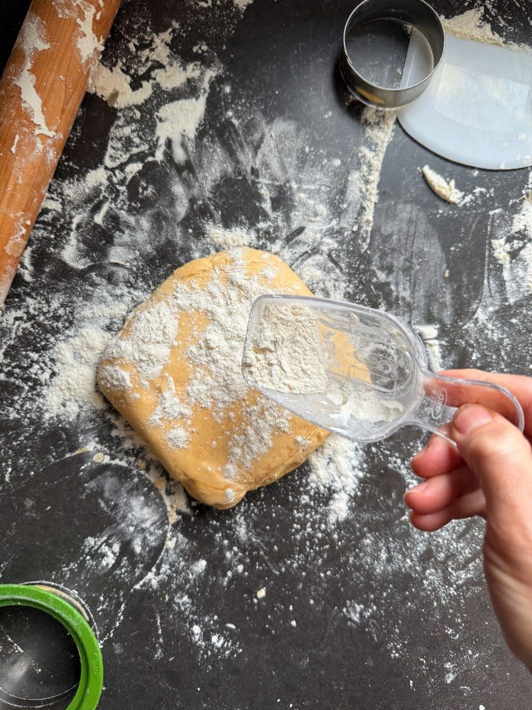 cookie dough on a floured countertop with a rolling pin and cookie cutters in the edge of the photo
