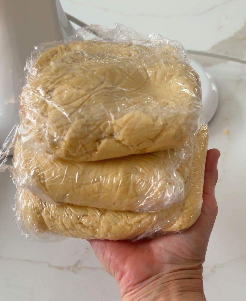 three plastic wrapped portions of cookie dough being held by a a hand
