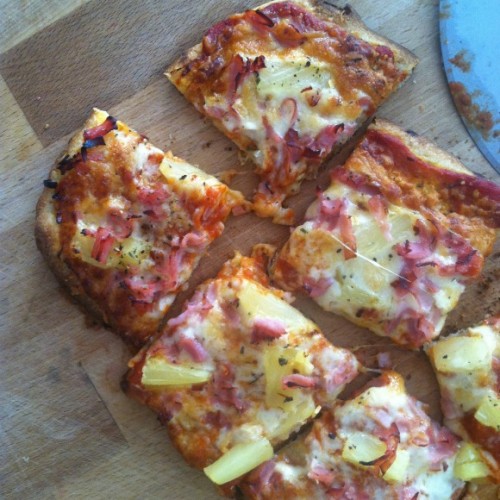 photo of ham and pineapple pizza cut into squares on a wood cutting board