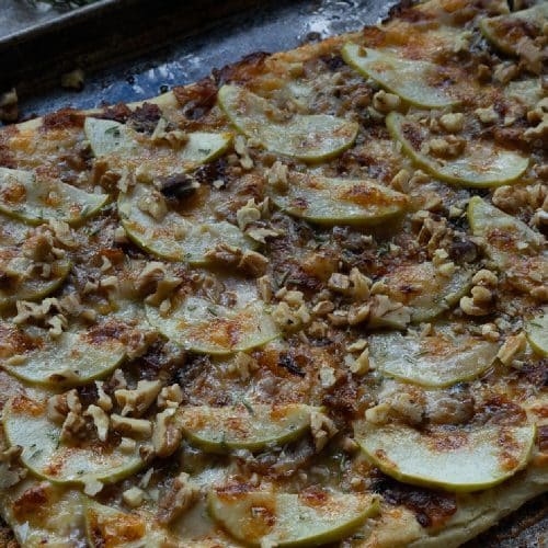apple and sharp cheddar pizza shows baked pizza with brown bubbly cheese on a sheet pan with an apple and a wood bowl of salt and rosemary sprig in the background