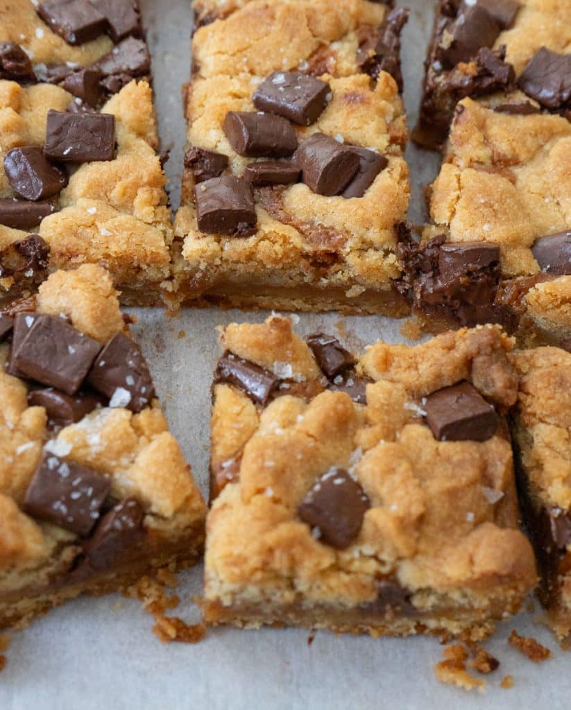 hands pulling apart a salted caramel chocolate chunk cookie bar over the pan of bars