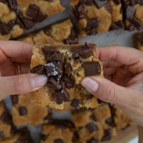 hands pulling apart a salted caramel chocolate chunk cookie bar over the pan of bars