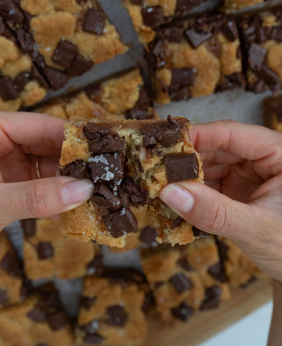 hands pulling apart a salted caramel chocolate chunk cookie bar over the pan of bars
