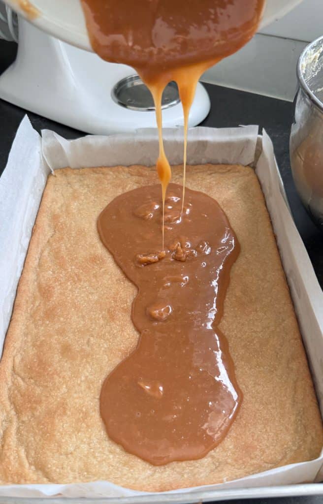 pouring caramel over the bottom shortbread layer of the sea salt caramel chocolate chunk bars
