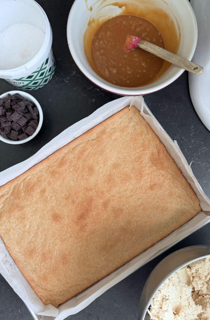 baked bottom layer of salted cookie bars with the components to finish the recipe sitting on the counter around the pan