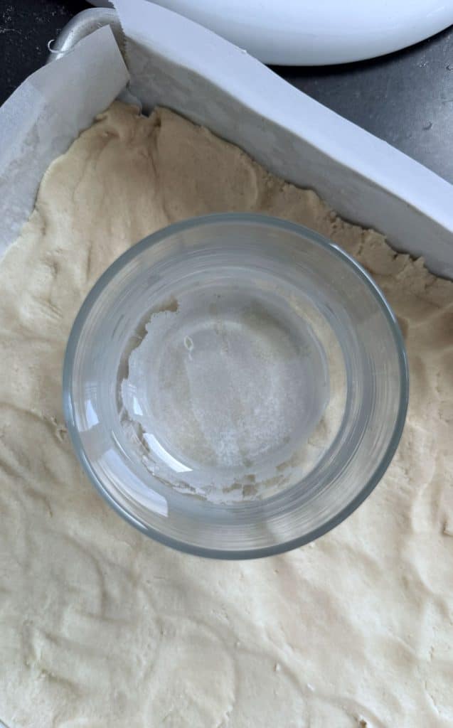pressing shortbread dough into the bottom of baking pan lined with parchment paper