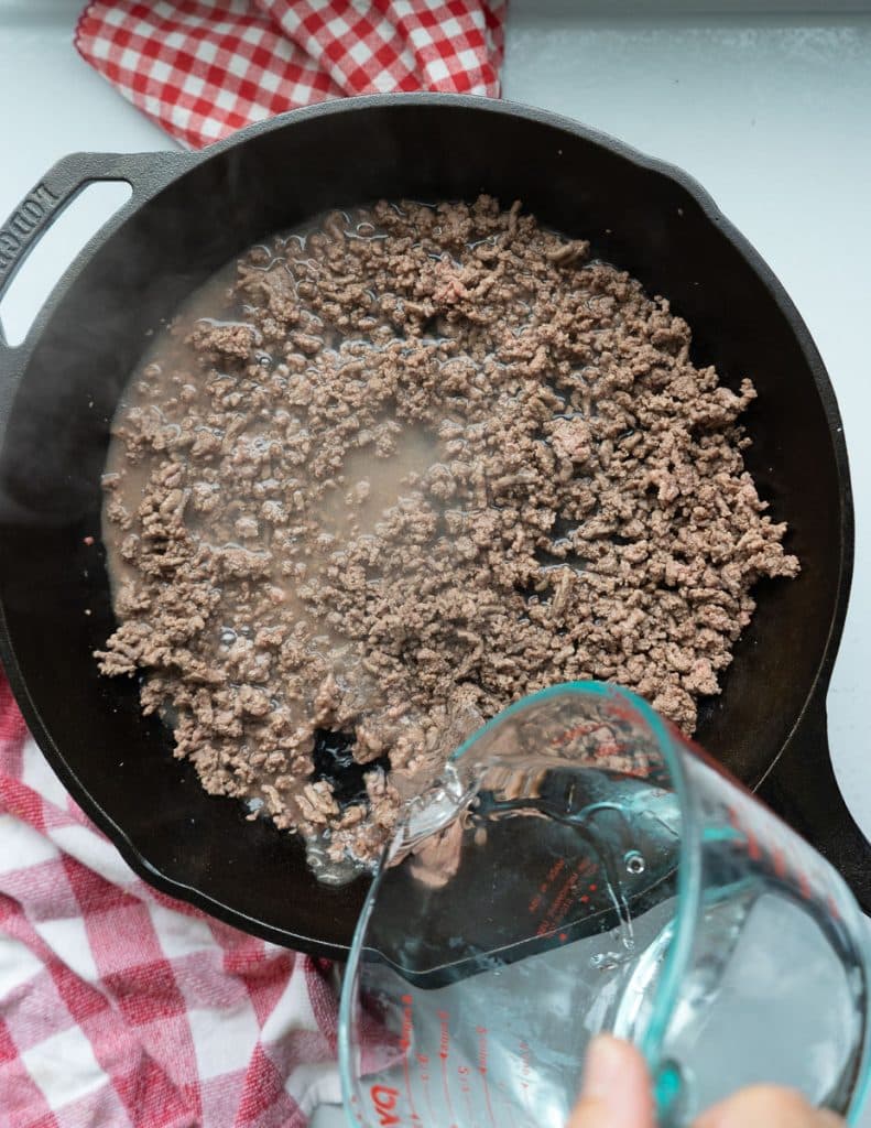 adding water to browned ground beef in a cast iron skillet