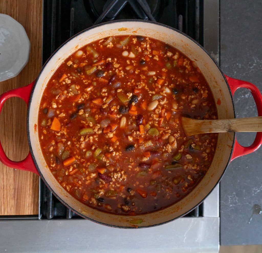 pot of three bean turkey soup in a dutch oven with a wood spoon in the soup. pot is on the stovetop