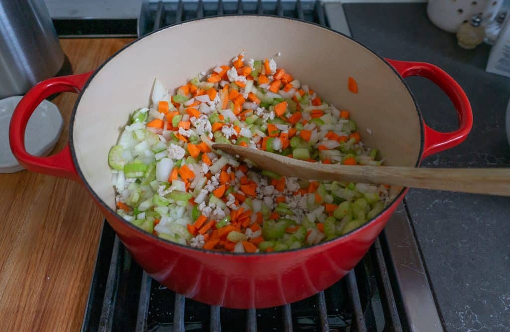 adding chopped vegetables like carrots, onions, and celery to cooked ground turkey in dutch oven on stovetop