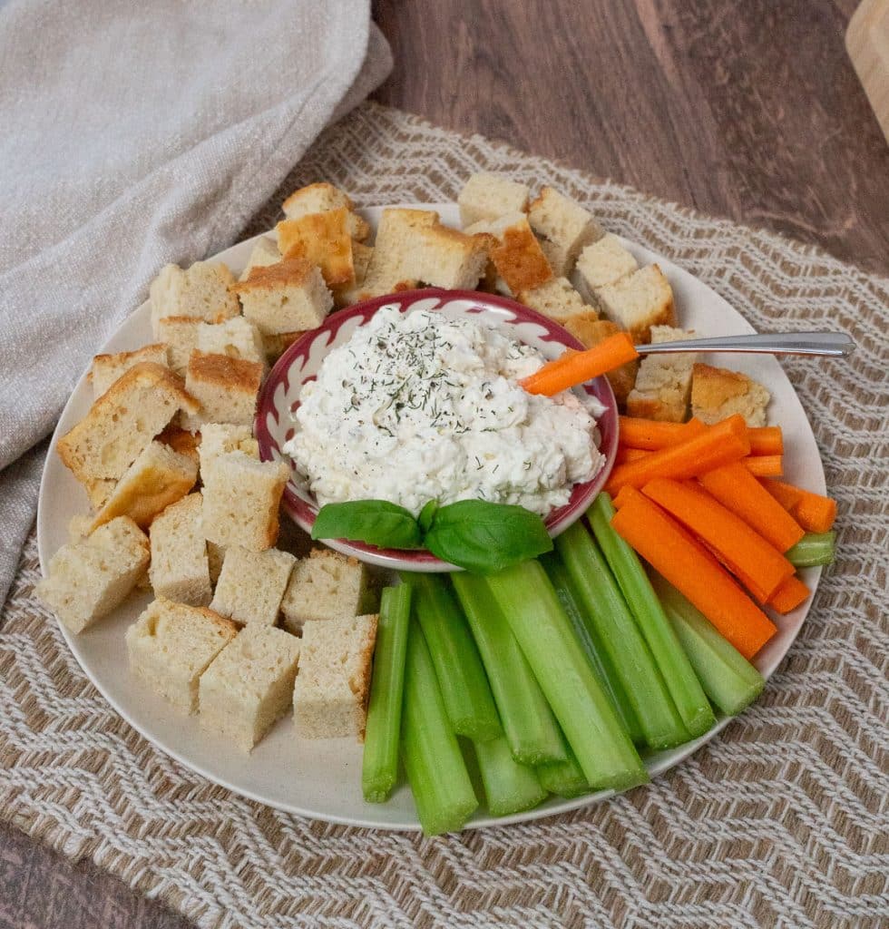 dish of feta herb dip in the middle of a plate surrounded by celery, carrots and chunks of bread