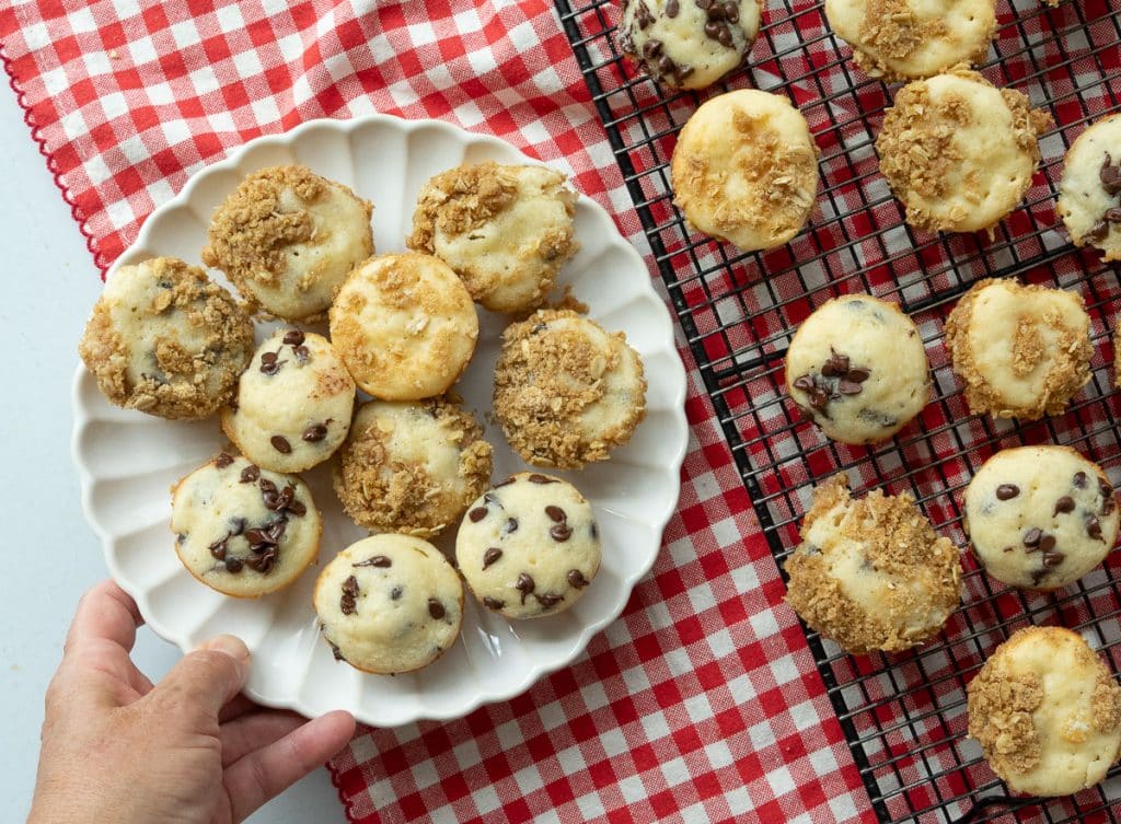 plate of mini muffins on a white plate on a red and white gingham cloth next to a cooling rack of mini muffins